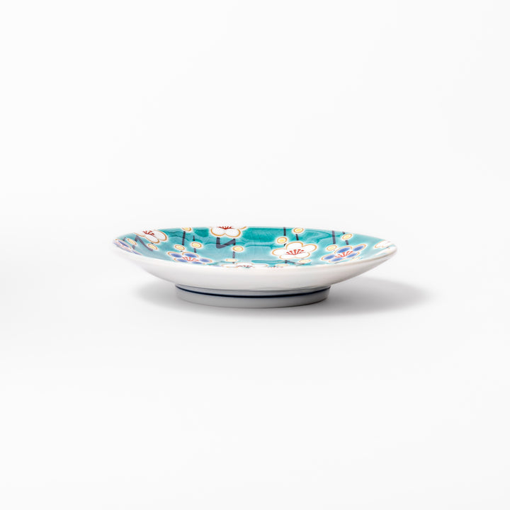 Round Japanese ceramic sauce dish with teal background, decorated with white and blue plum blossom motifs, perfect for serving condiments or small bites.