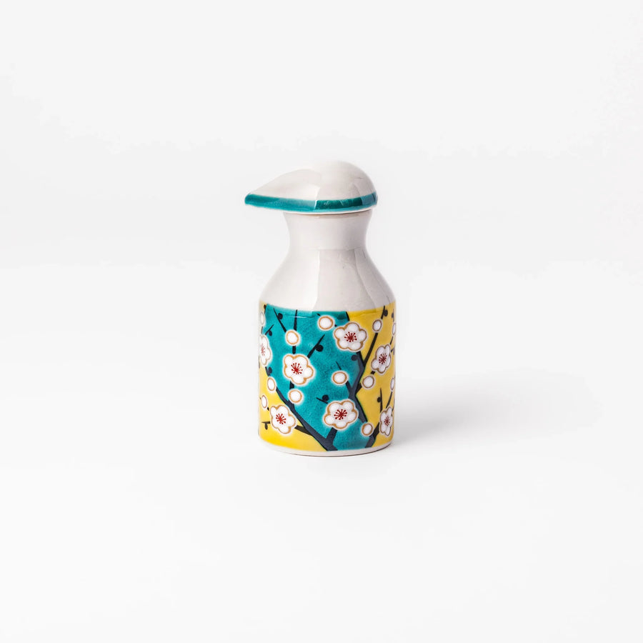 Japanese porcelain soy sauce dispenser with white plum blossoms on yellow and teal background, handcrafted spring design.