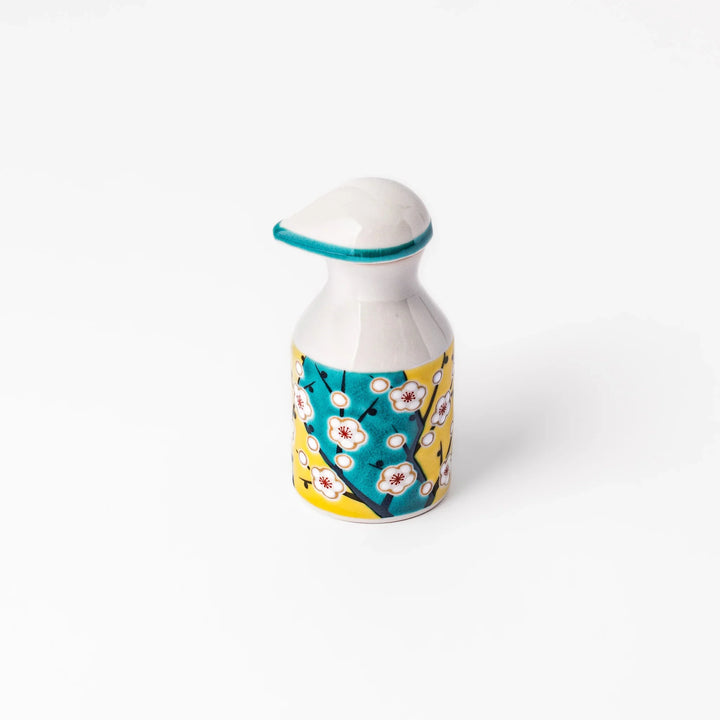 Japanese porcelain soy sauce dispenser with white plum blossoms on yellow and teal background, handcrafted spring design.