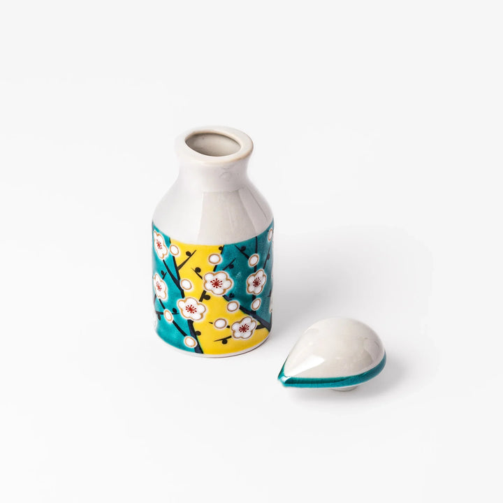 Japanese porcelain soy sauce dispenser with white plum blossoms on yellow and teal background, handcrafted spring design.