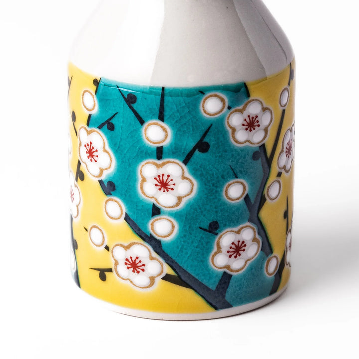 Japanese porcelain soy sauce dispenser with white plum blossoms on yellow and teal background, handcrafted spring design.