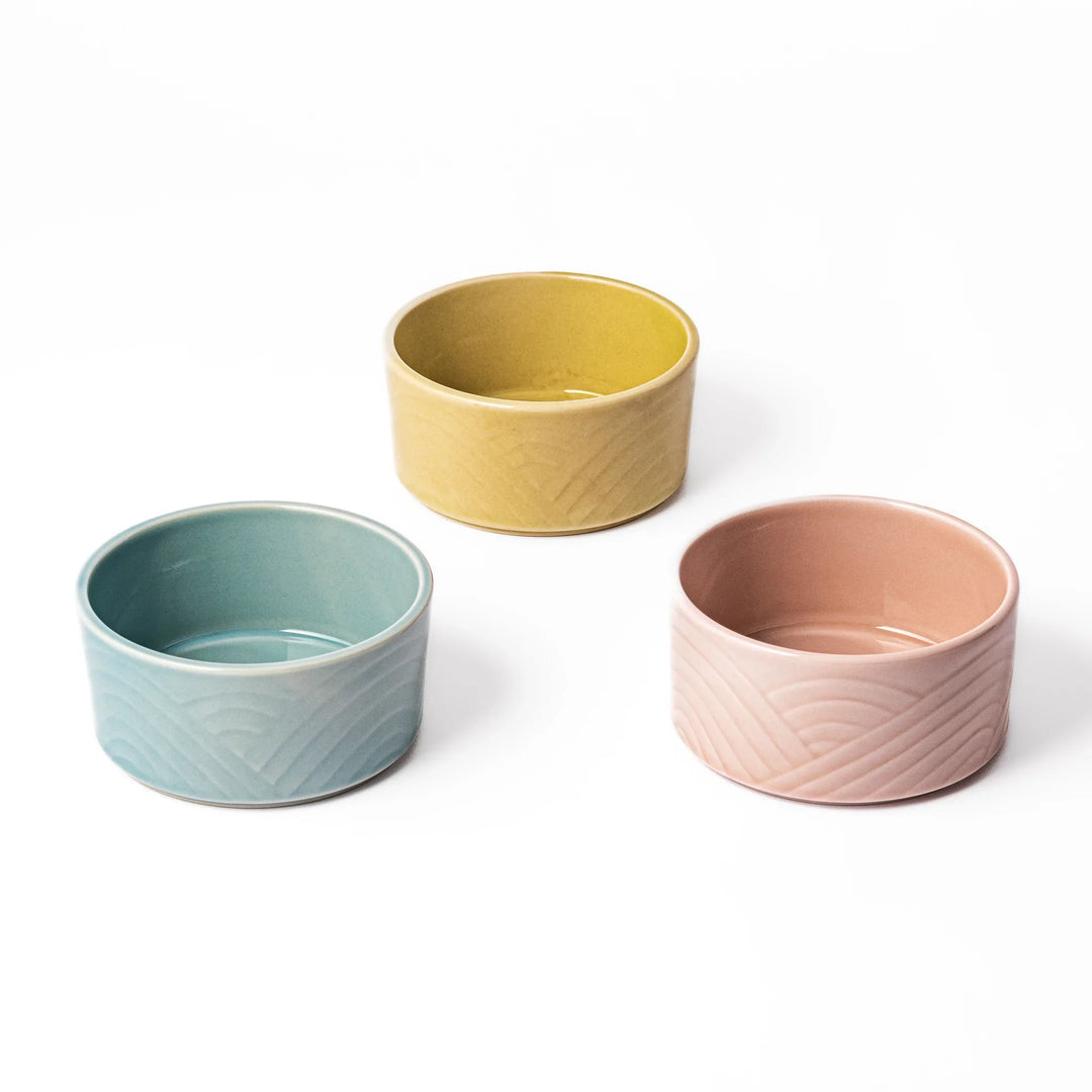 Three medium porcelain bowls in pastel blue, yellow, and pink, featuring embossed Seigaiha wave patterns and stackable design.