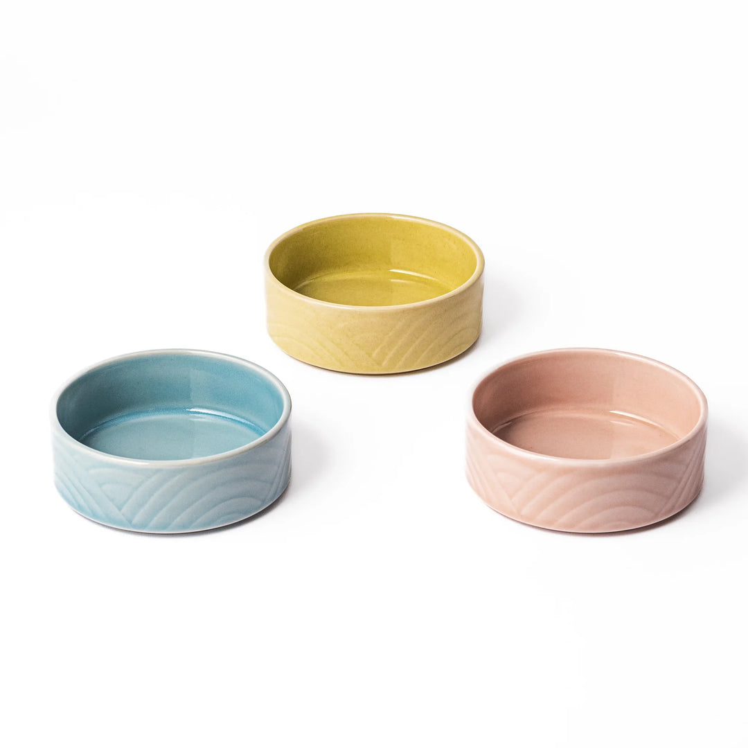 Three small porcelain bowls in yellow, pink, and blue, each embossed with gentle Seigaiha wave patterns for a modern Japanese touch.