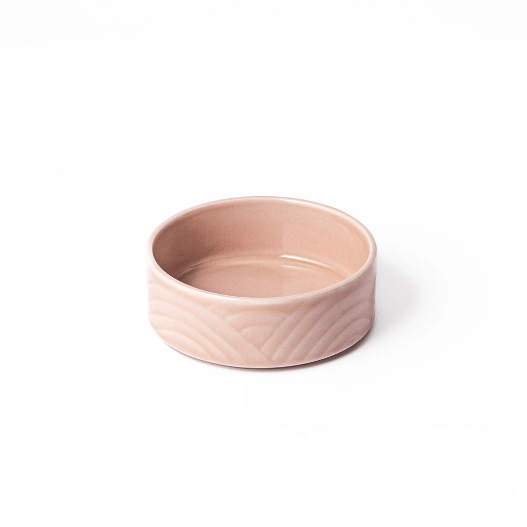 Light pink porcelain bowl with embossed Japanese wave pattern, simple cylindrical shape and glossy finish on a white background.