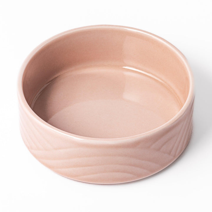 Light pink porcelain bowl with embossed Japanese wave pattern, simple cylindrical shape and glossy finish on a white background.