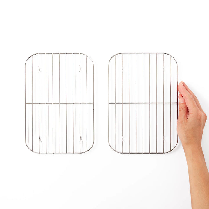 Hand holding one of two large Japanese stainless steel prep tray wire racks for size comparison