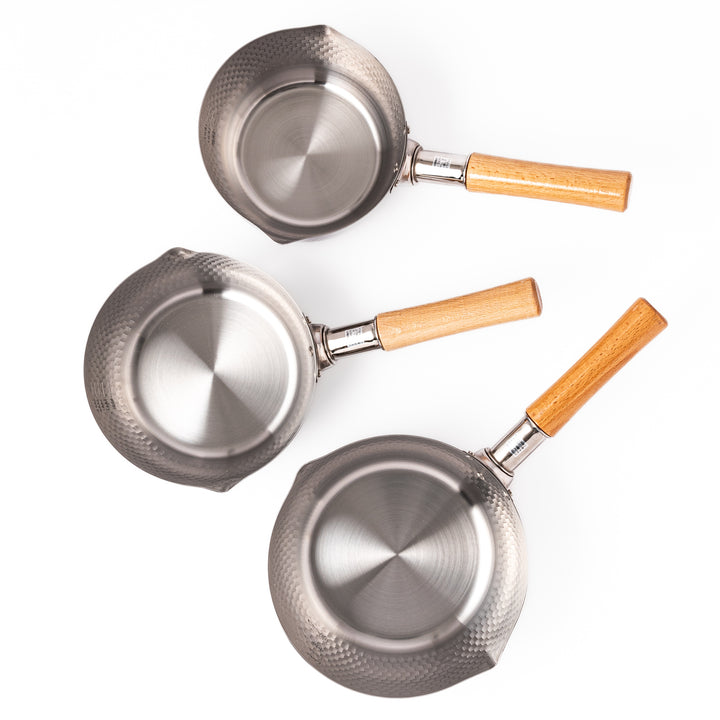 Three Japanese stainless steel Yukihira pots with hammered texture and wooden handles, showcasing durable craftsmanship for everyday soups and simmered dishes.