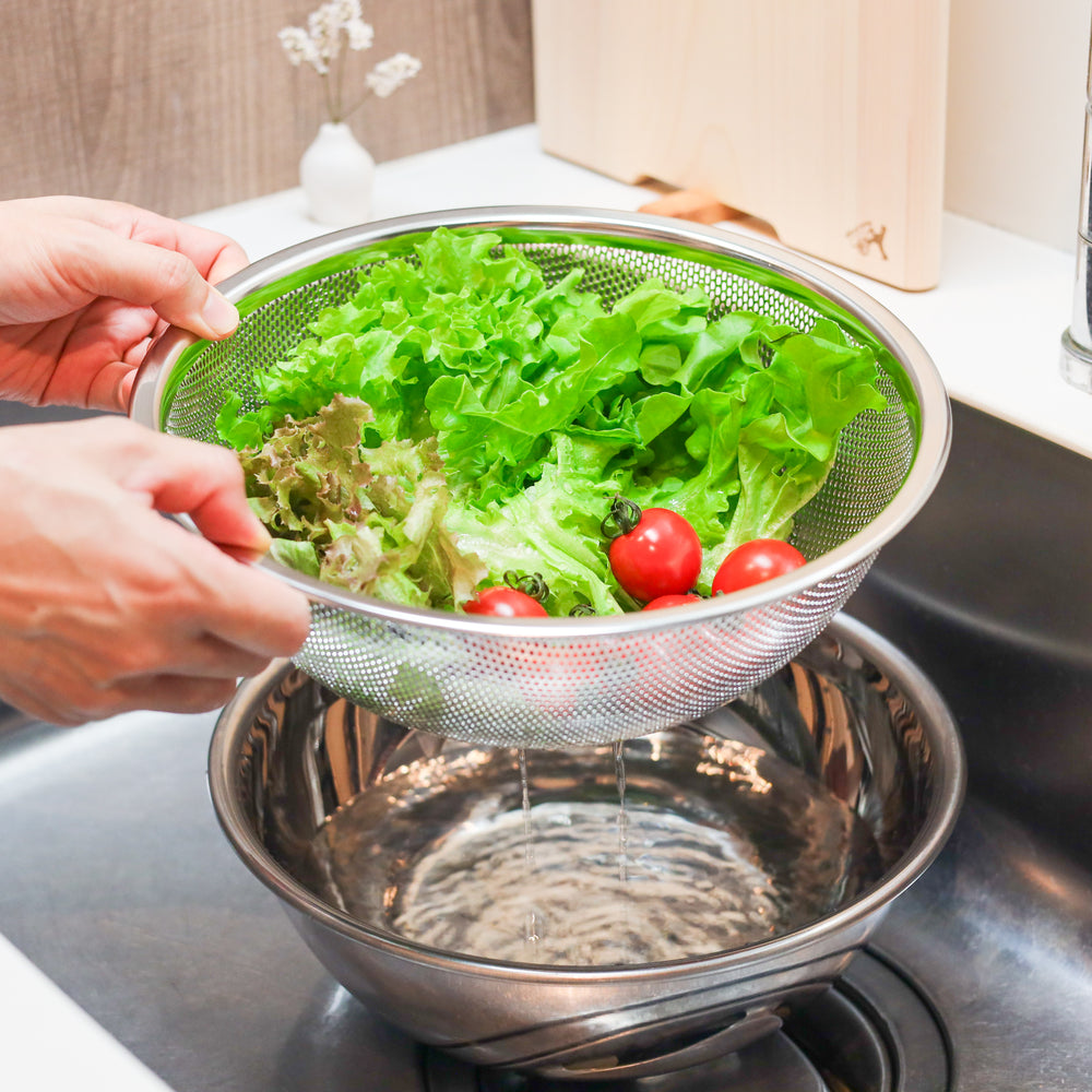 Washed lettuce and tomatoes draining in a colander over a bowl, showing efficient rinsing and straining in kitchen workflow.