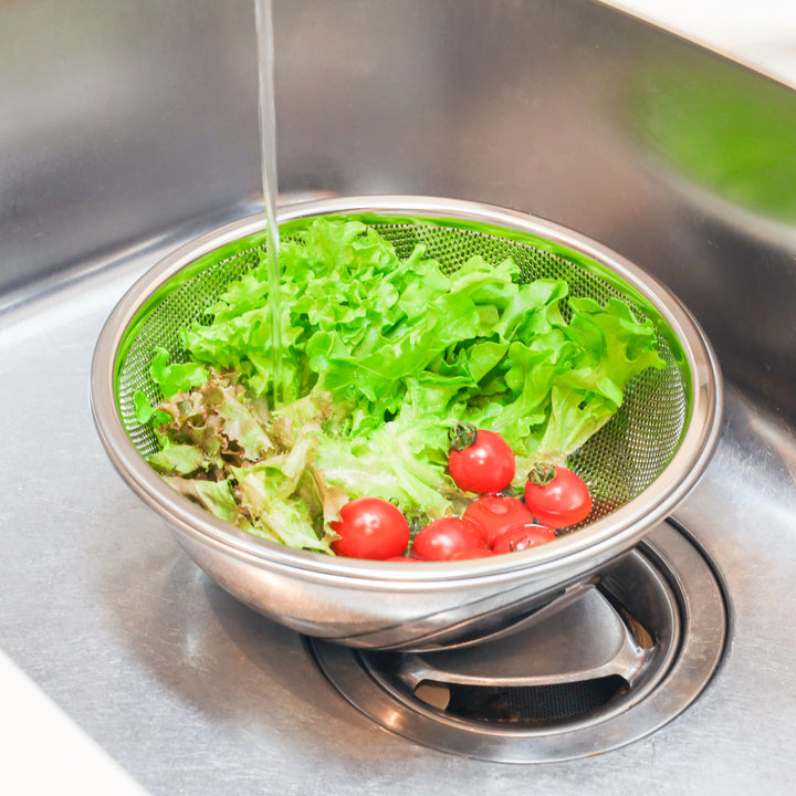 Fresh lettuce and tomatoes being rinsed in a stainless steel colander, perfect for salad prep and everyday vegetable washing.