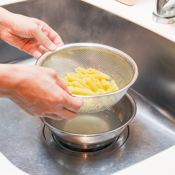 Boiled penne being drained in a stainless steel colander over a bowl, ideal for efficient cooking and water-saving prep.
