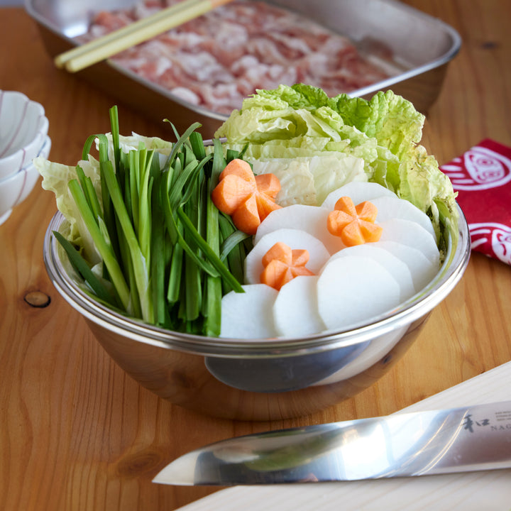 Stainless steel mixing bowl filled with napa cabbage, daikon, carrots, and garlic chives prepared for Japanese hot pot cooking.
