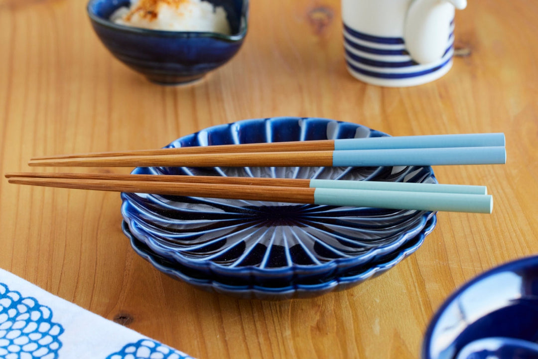 Light blue and mint chopsticks resting on deep blue ceramic plates on a wooden table, creating a bright and modern table setting.