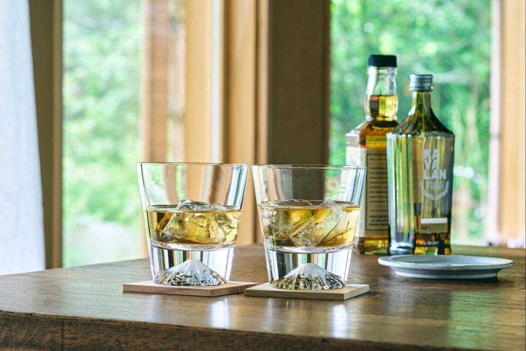 Mt Fuji base whiskey glasses with ice and golden liquor on a wooden table with bottles in the background