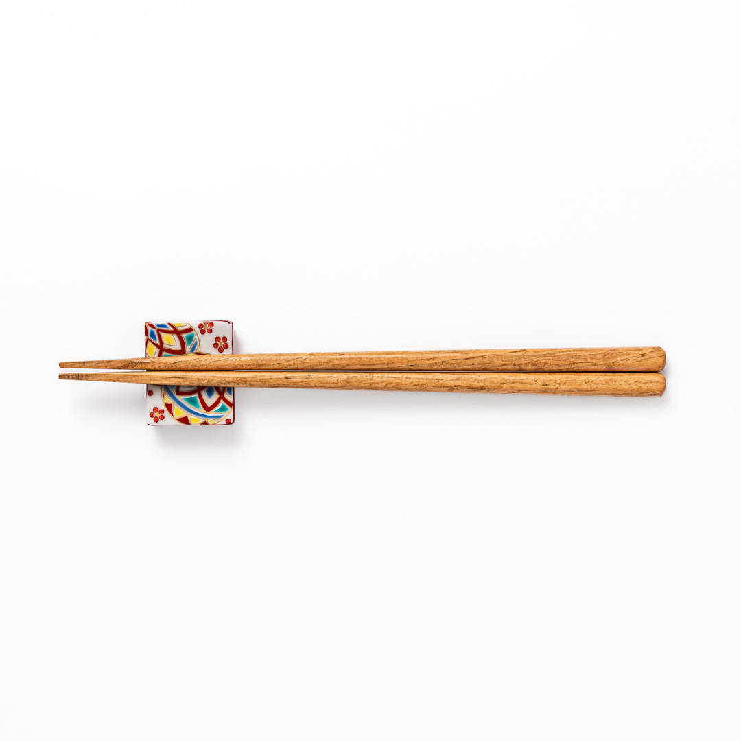 Rectangular Japanese ceramic chopstick rest adorned with colorful temari ball patterns and red floral accents, bringing vibrant charm to any dining table.