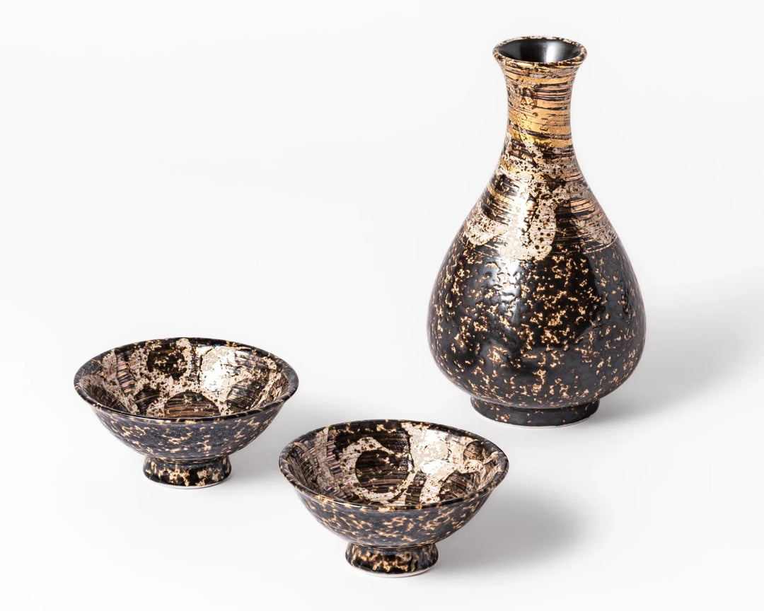 Black and gold ceramic sake set with a tall tokkuri and two cups on a white background