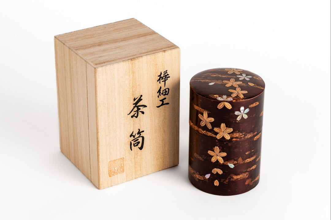 Handcrafted tea caddy with sakura inlay displayed beside its wooden storage box on a clean white background