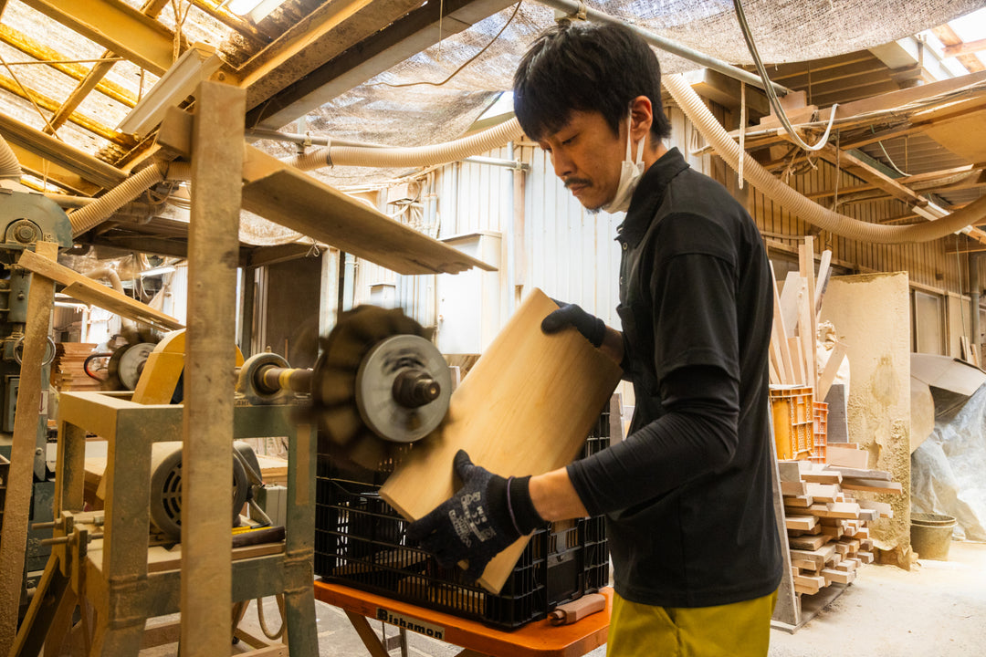 Craftsman sanding a wooden board in a workshop, shaping smooth surfaces with a rotating machine and skilled hands.