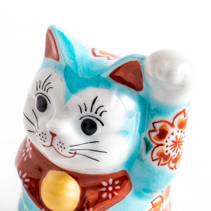 Vibrant Turkish blue Maneki Neko figurine adorned with floral patterns in orange and white, featuring a golden bell and a raised paw, symbolizing good fortune and prosperity.