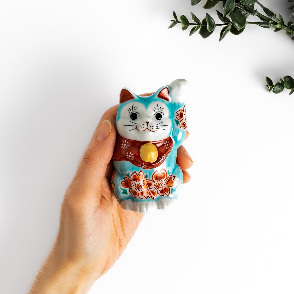 Vibrant Turkish blue Maneki Neko figurine adorned with floral patterns in orange and white, featuring a golden bell and a raised paw, symbolizing good fortune and prosperity.