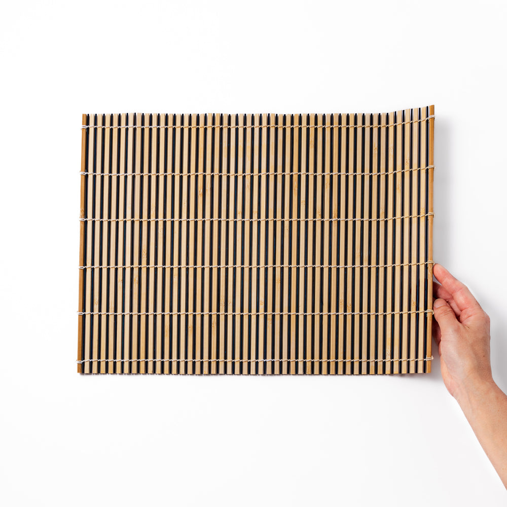 Two-tone bamboo table mat with alternating light and dark slats, tightly woven with white cord—ideal for adding texture to your Japanese table setting.