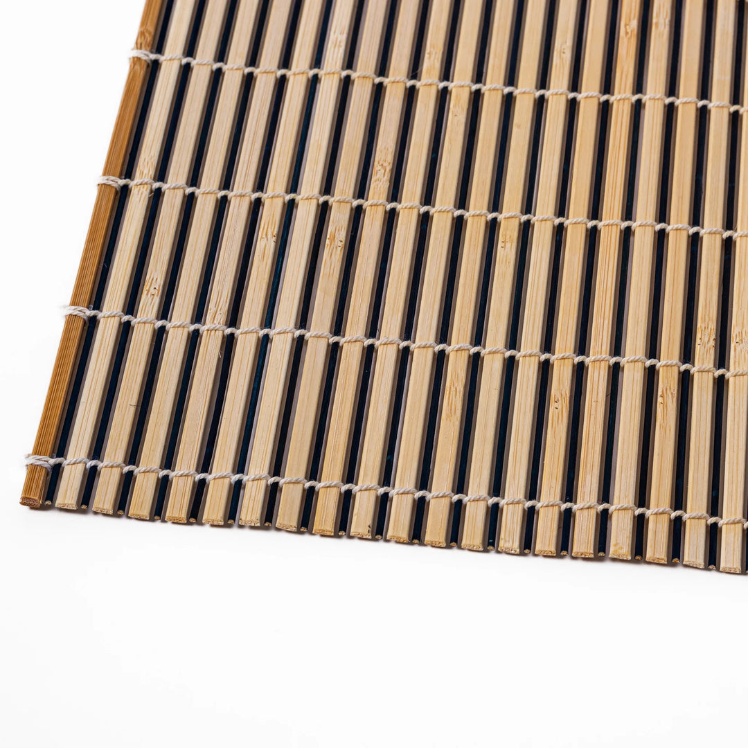 Two-tone bamboo table mat with alternating light and dark slats, tightly woven with white cord—ideal for adding texture to your Japanese table setting.