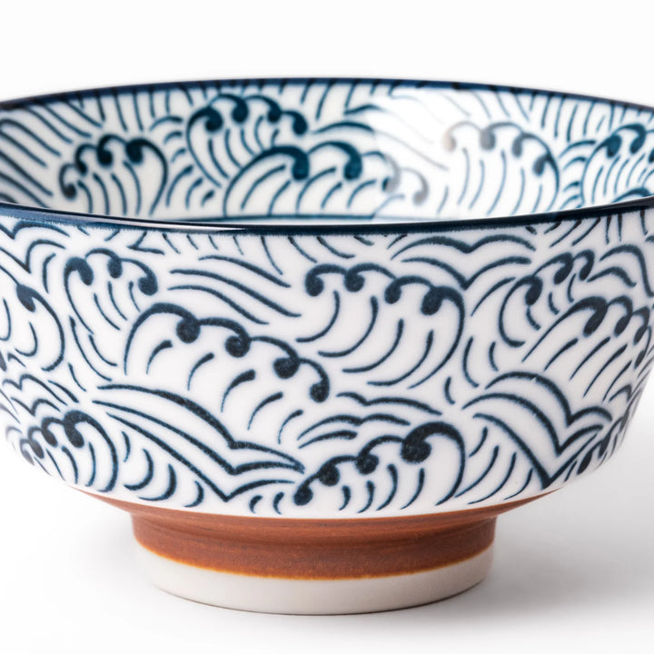 White porcelain rice bowl with navy blue wave ripple pattern and unglazed brown base, photographed on a white background.