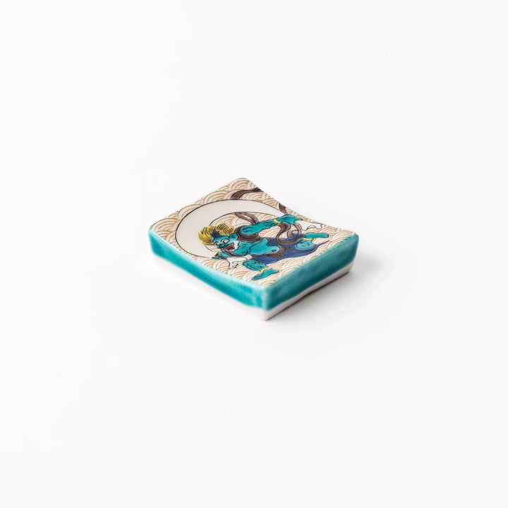 Japanese porcelain chopstick rest featuring the Wind God design with blue figure and gold wave pattern background.