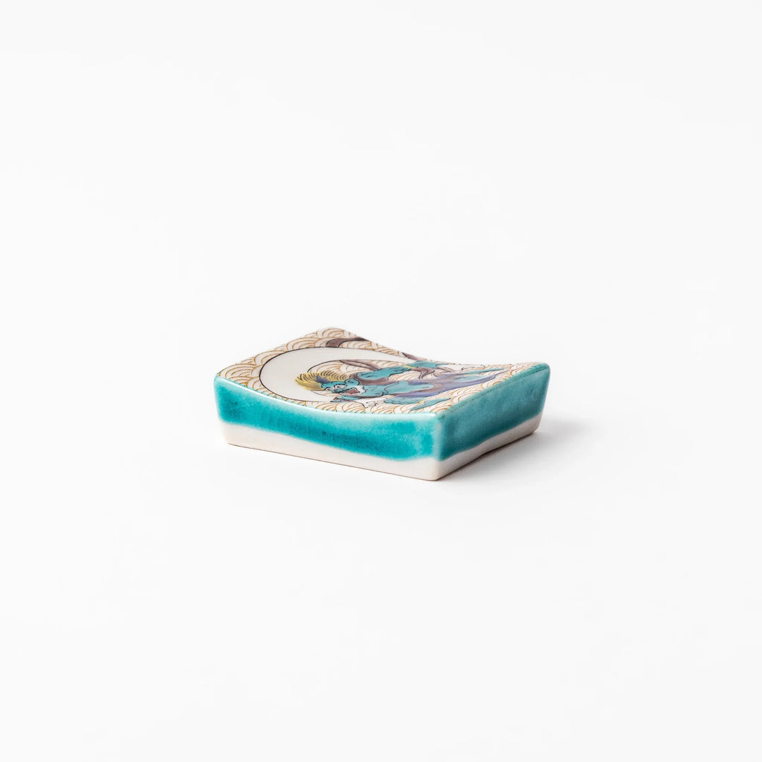 Japanese porcelain chopstick rest featuring the Wind God design with blue figure and gold wave pattern background.