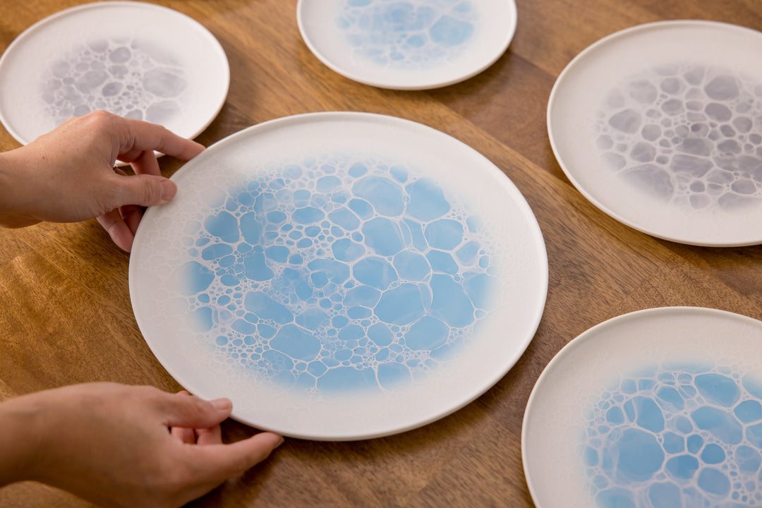 Large ceramic plates with blue bubble-pattern glaze being arranged on a wooden table.