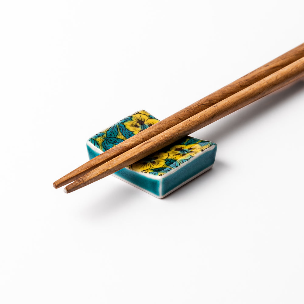 Rectangular Japanese ceramic chopstick rest decorated with vivid yellow floral design and teal leaves, bringing elegance and color to your dining table.