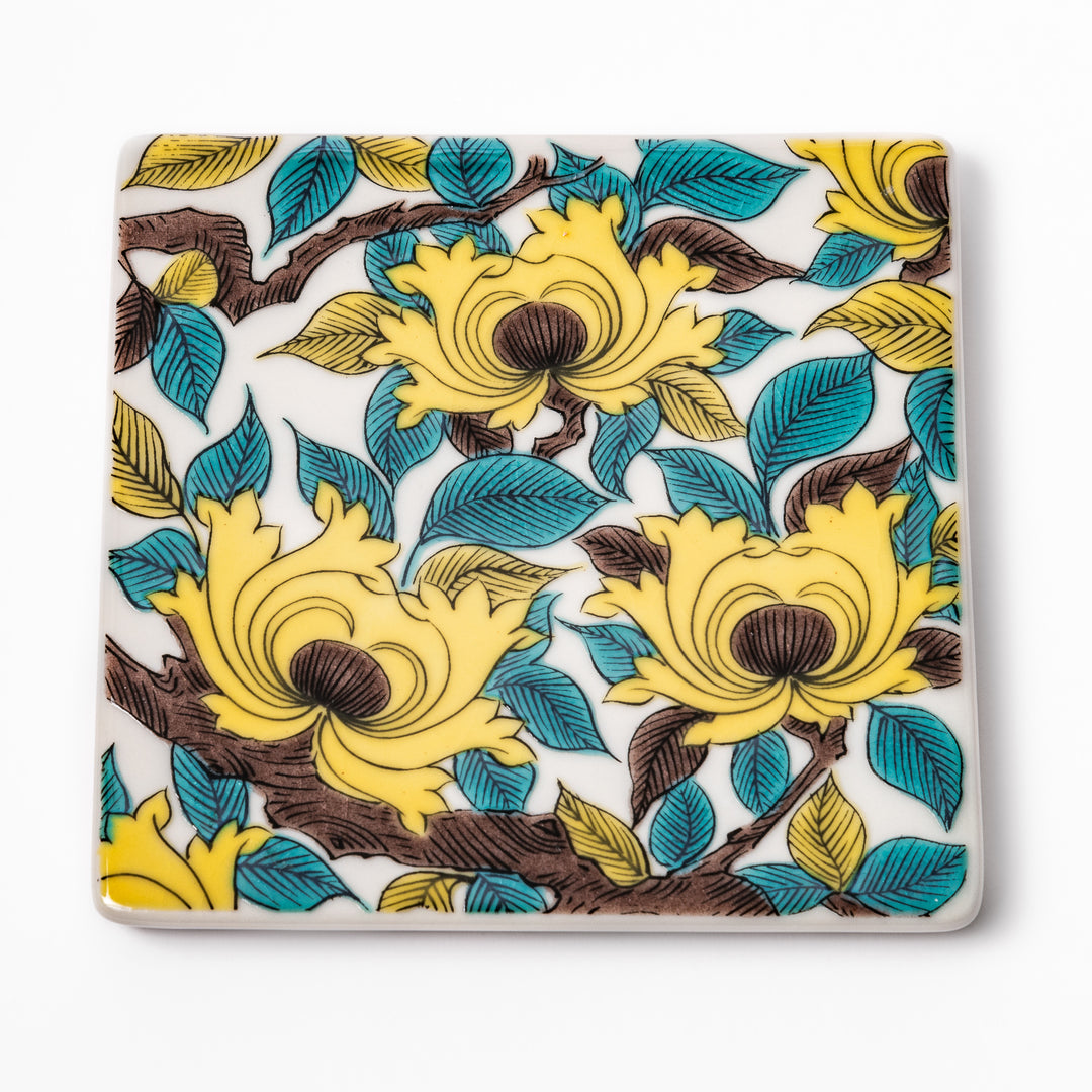 Square Japanese ceramic coaster adorned with vivid yellow peony blooms and teal leaves, adding elegance and charm to any dining table setting.