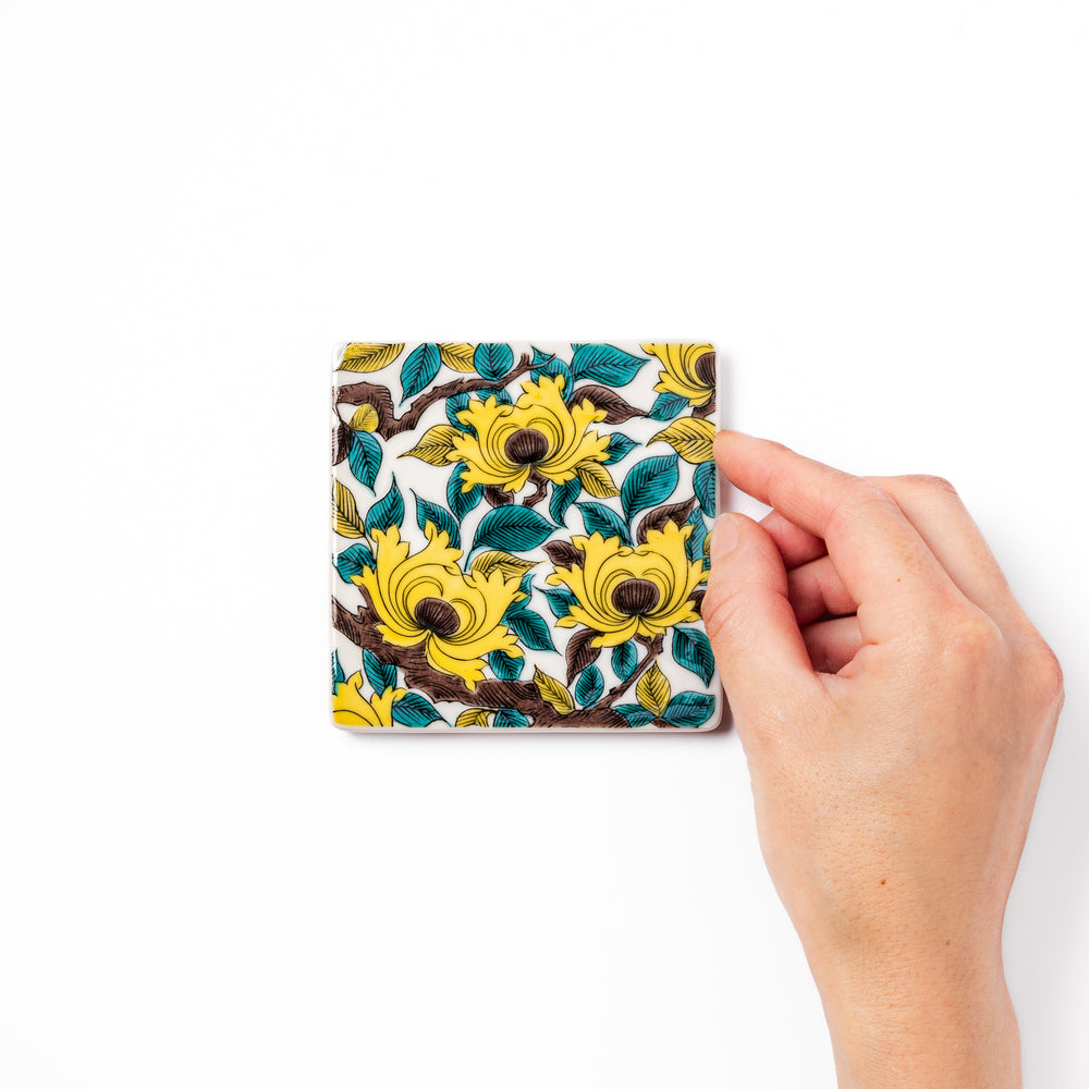 Square Japanese ceramic coaster adorned with vivid yellow peony blooms and teal leaves, adding elegance and charm to any dining table setting.