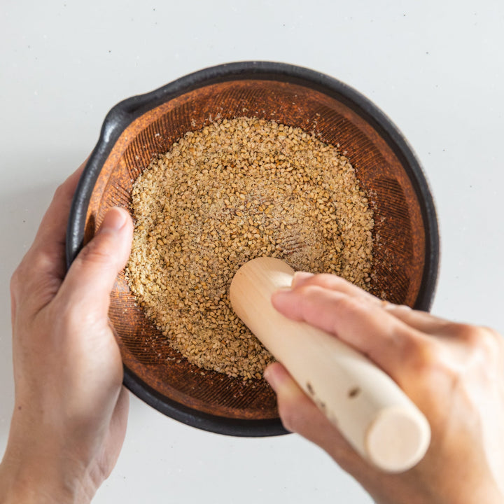 Japanese suribachi mortar and wooden pestle grinding toasted sesame seeds for fresh aromatic seasoning