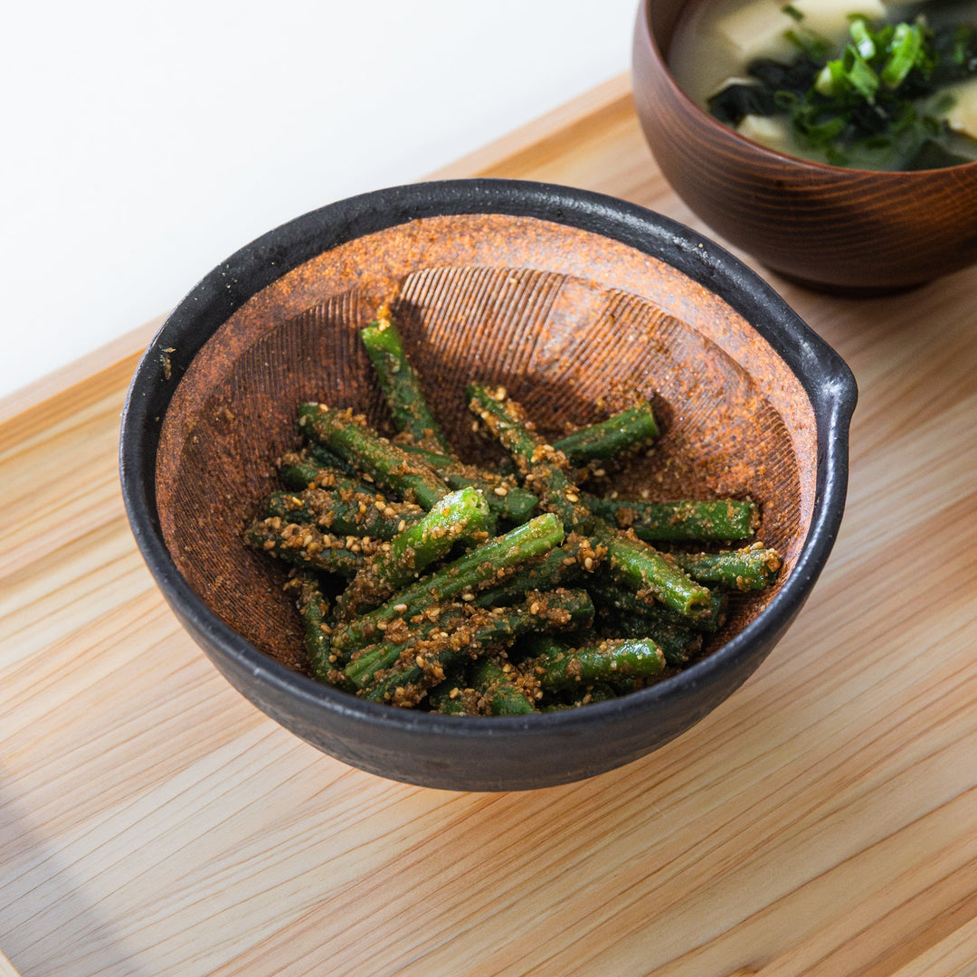 Japanese suribachi mortar with sesame dressed green beans showing textured ridges and black ceramic finish