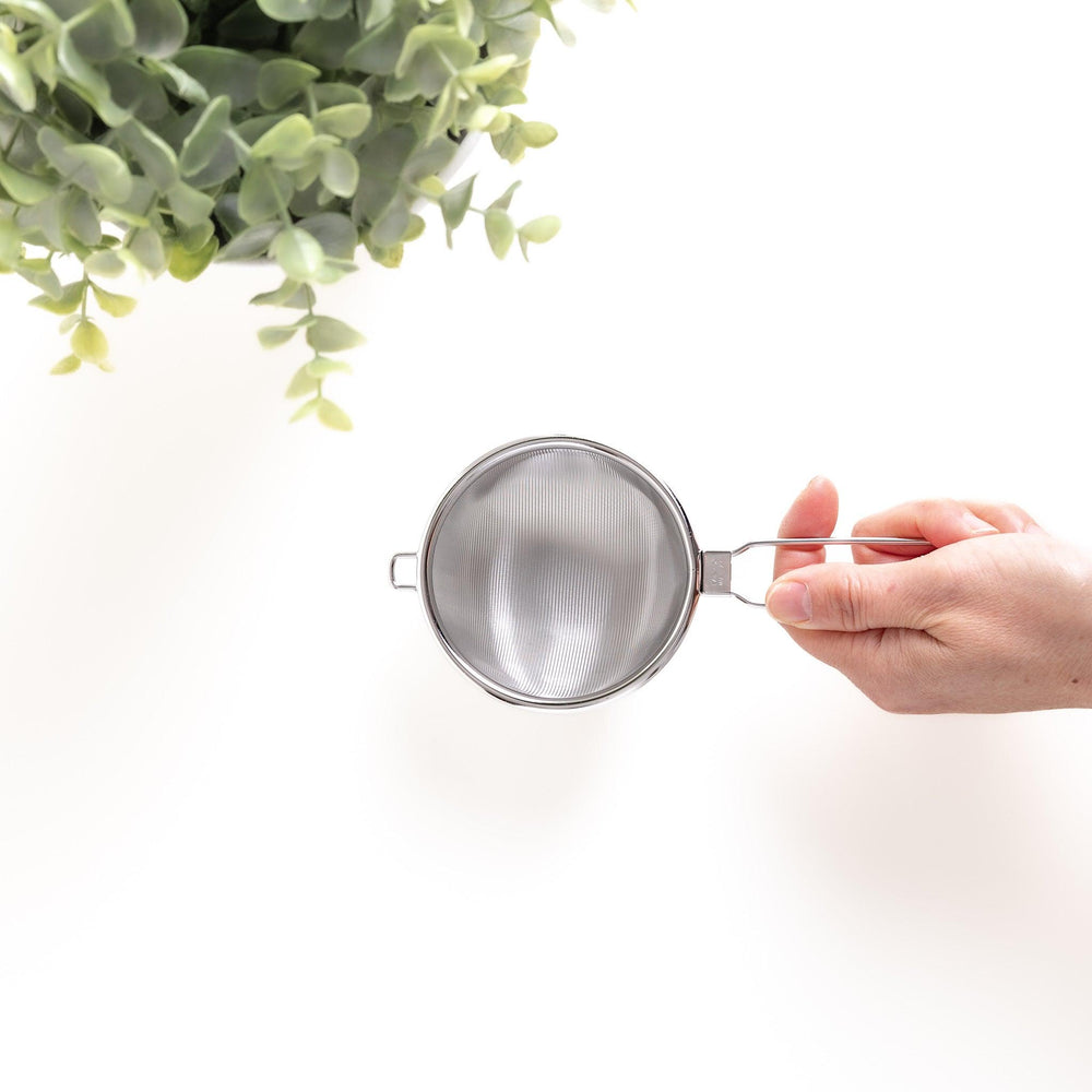 Hand holding a stainless steel tea strainer with a fine mesh and convenient handle, a versatile kitchenware tool for brewing loose leaf tea.