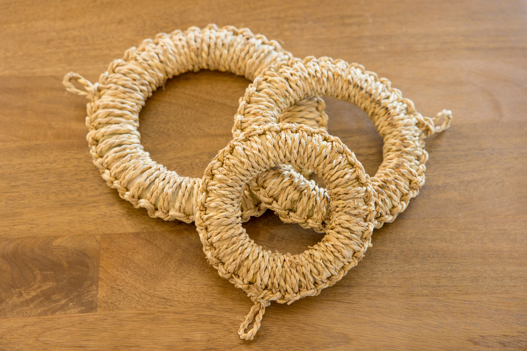 Natural woven straw trivets in three sizes handcrafted from rice straw displayed on a wooden table for kitchen use