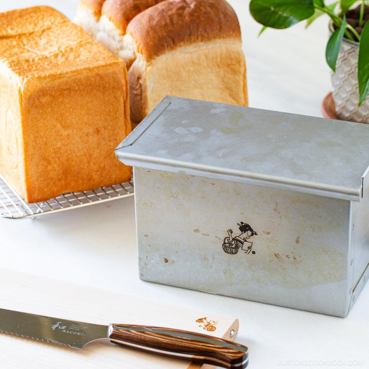 Japanese shokupan loaf pan used to bake milk bread loaves with golden crust on cooling rack with bread knife