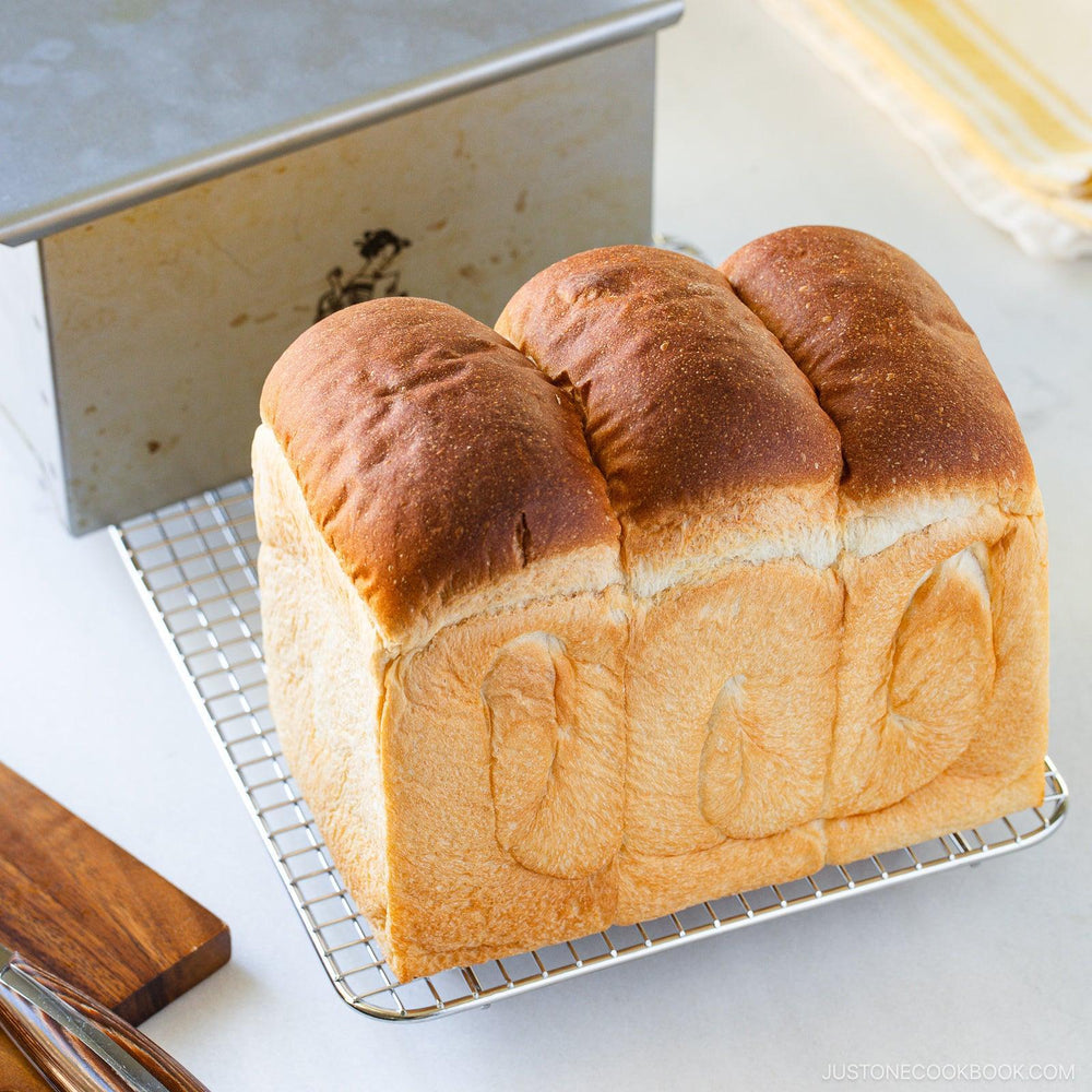 Close up Japanese shokupan milk bread loaf on cooling rack with soft airy crumb and golden brown top