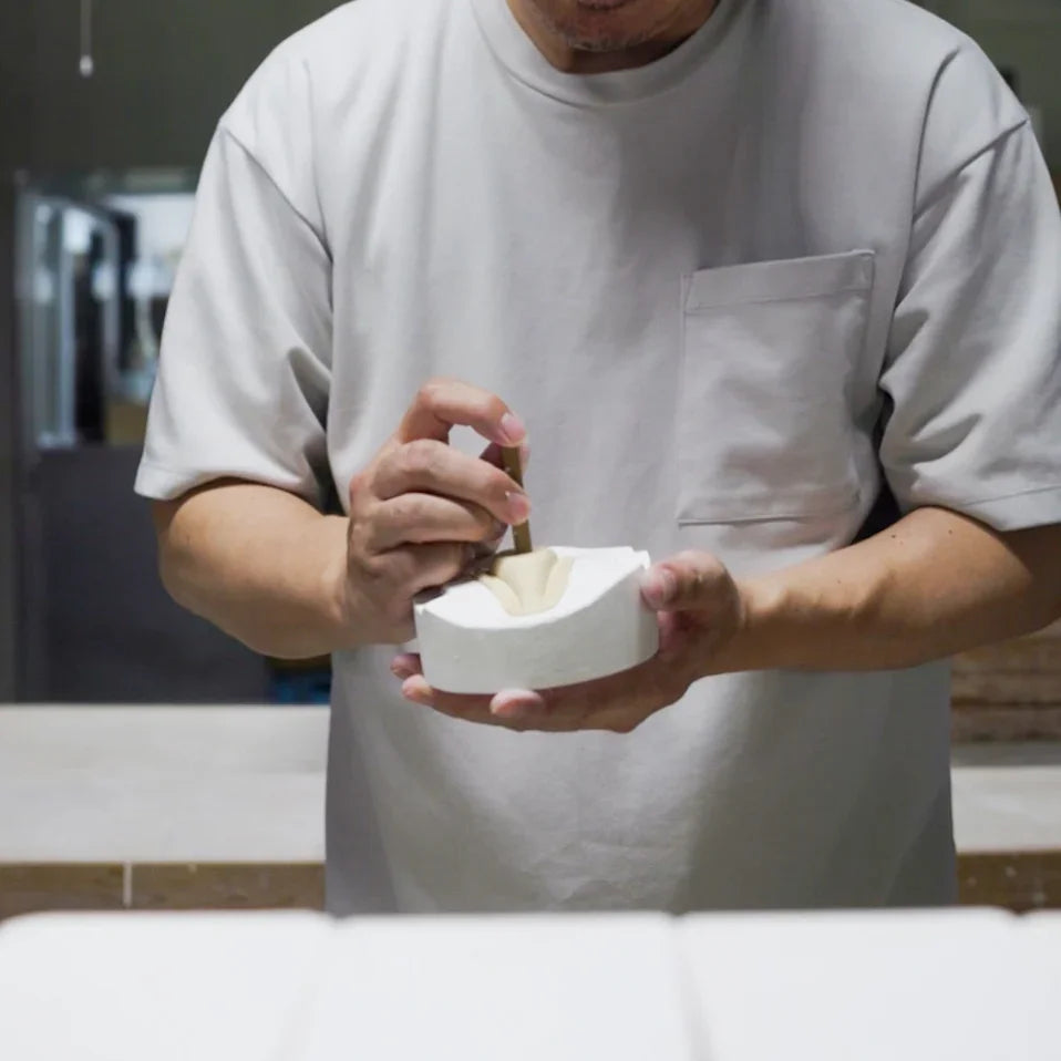 Artisan forming a clay piece inside a plaster mold with careful hand pressure in a traditional pottery workshop