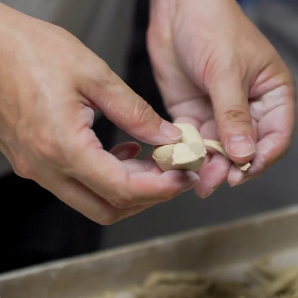Artisan refining a small clay piece by hand during detailed shaping work in a traditional pottery studio