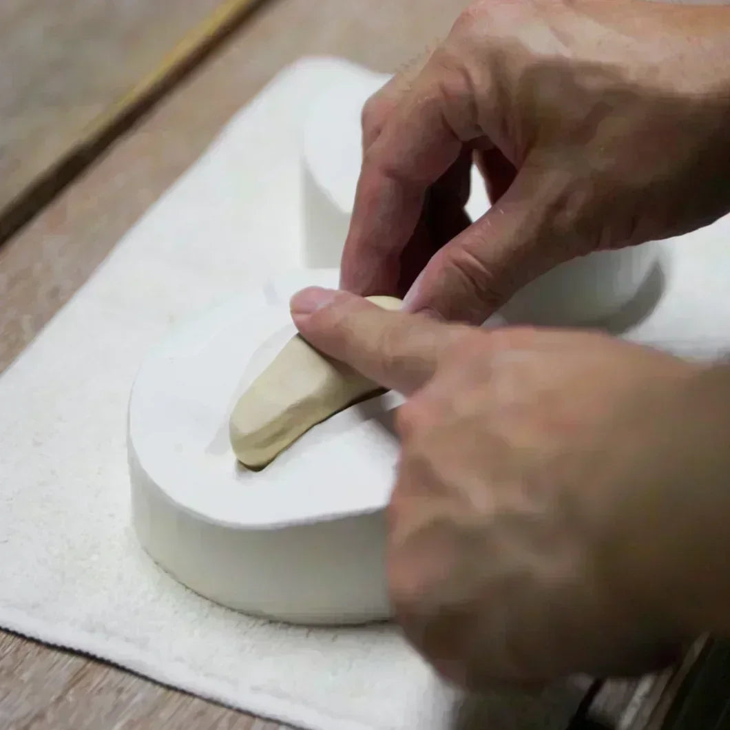 Artisan pressing clay into a plaster mold to shape a piece with careful handwork in a pottery workshop