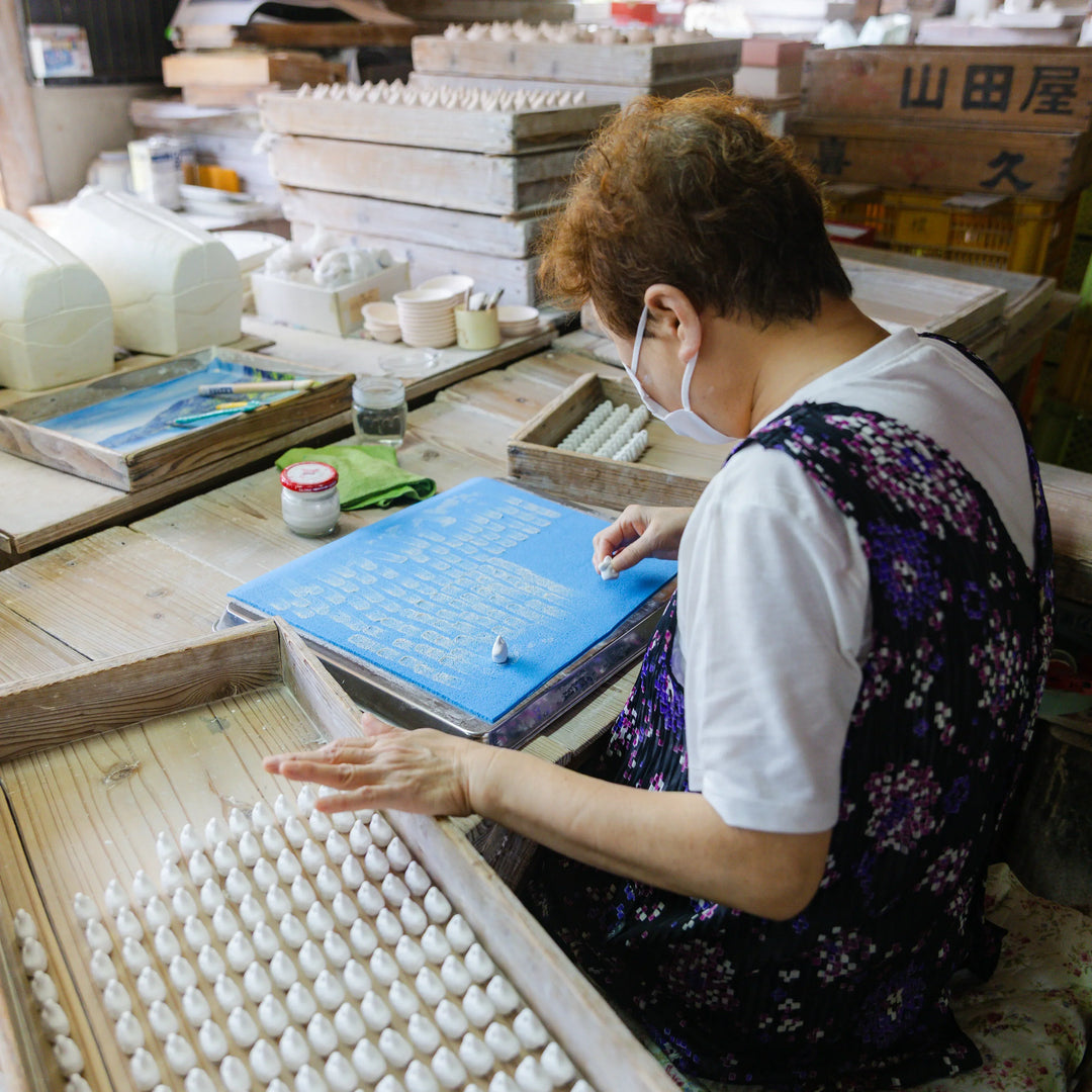 Artisan arranging small ceramic pieces on trays in the workshop during detailed preparation for pottery production