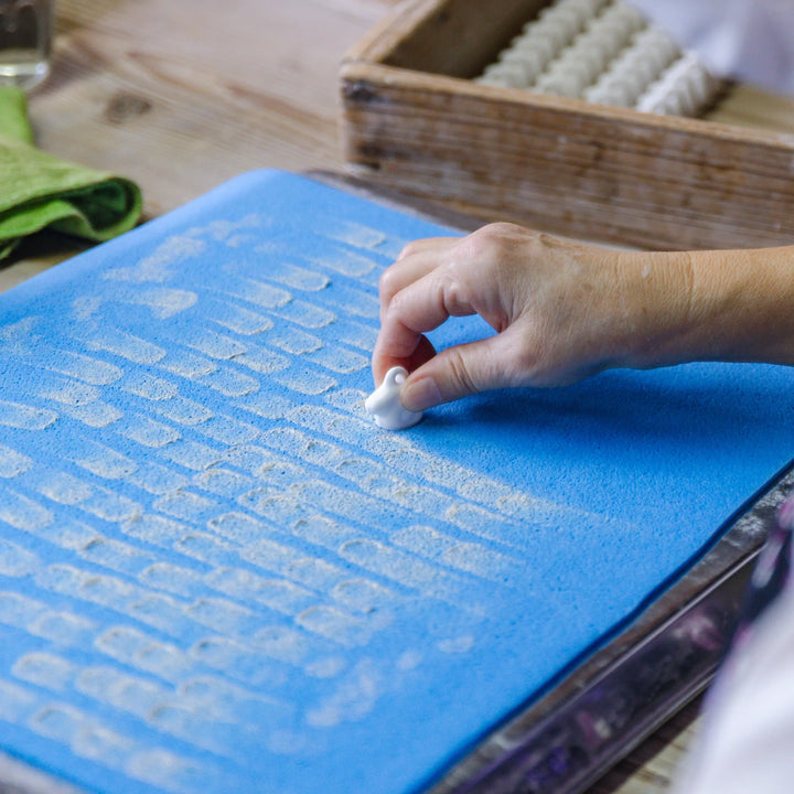 Artisan placing small ceramic pieces onto a padded tray with careful handwork during pottery preparation