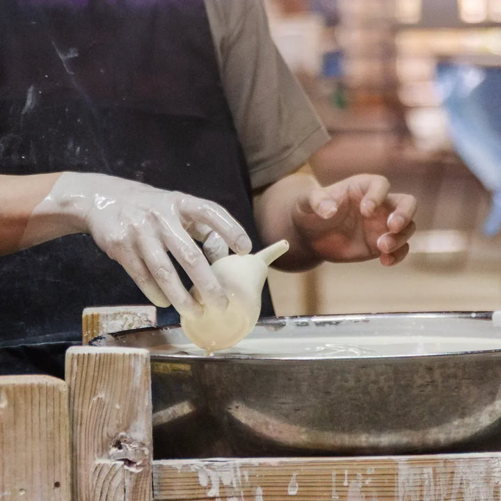Artisan dipping a clay vessel into white slip to coat its surface during the traditional pottery finishing process