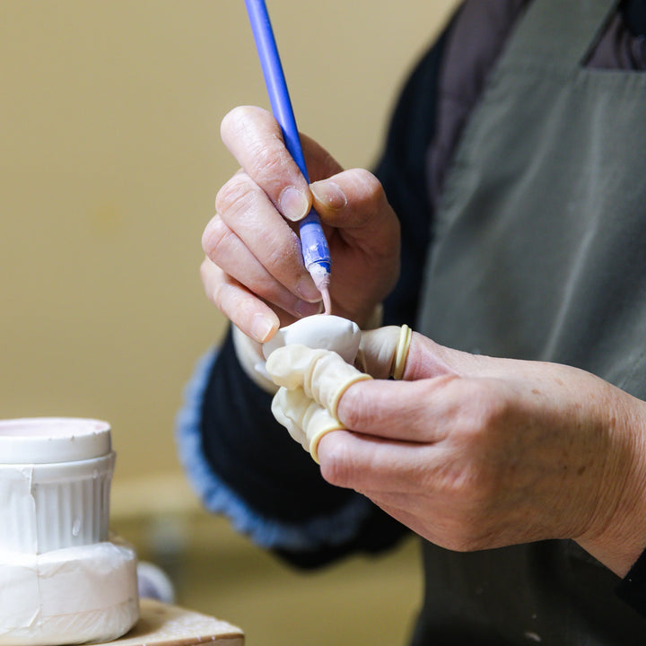 Artisan applying colored slip to a small ceramic piece with a brush during detailed hand painting work