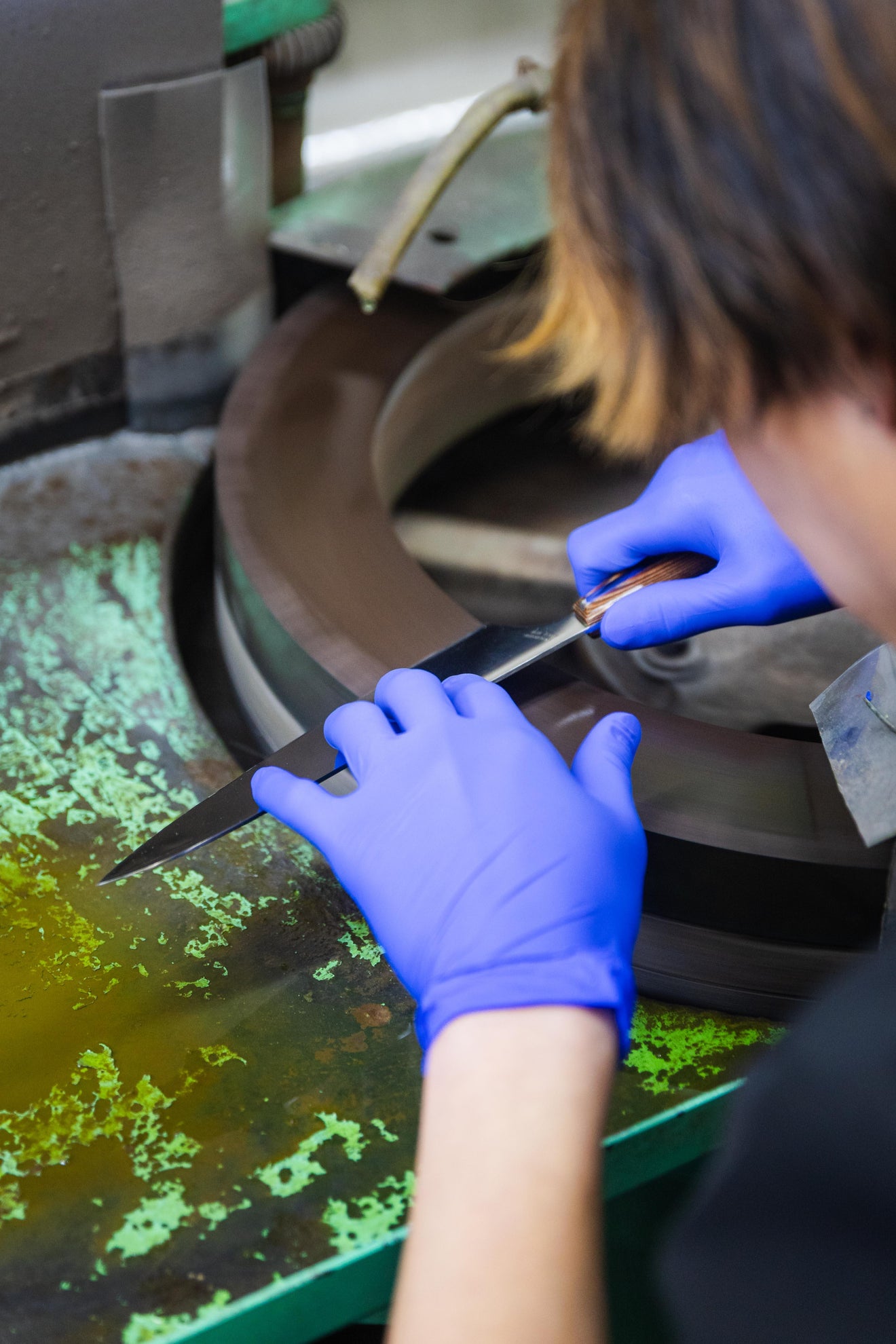 Japanese kitchen knife being sharpened by an artisan at Mitsuboshi Cutlery using a large rotating grinding stone in Japan