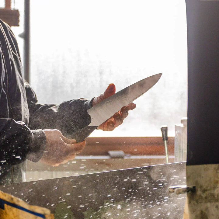 Artisan inspecting and rinsing a kitchen knife blade during the polishing process in the workshop