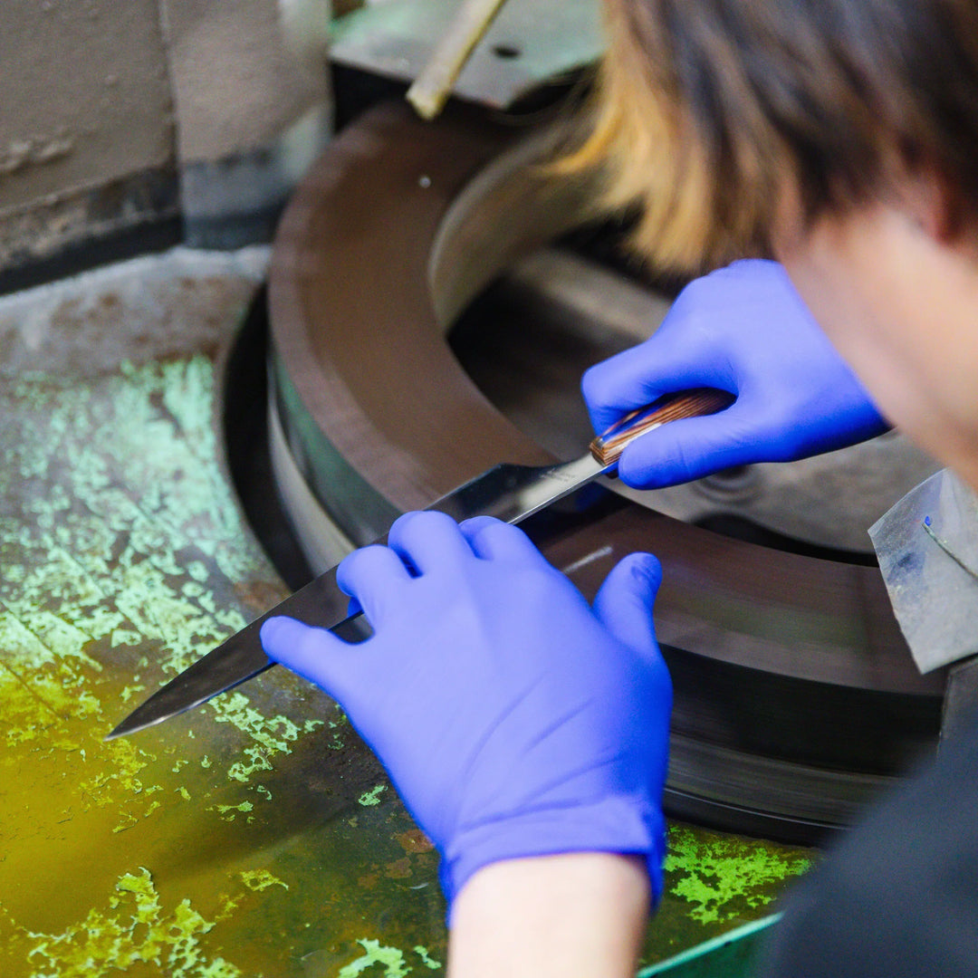 Artisan sharpening a kitchen knife blade on a rotating stone wheel with precise hand control