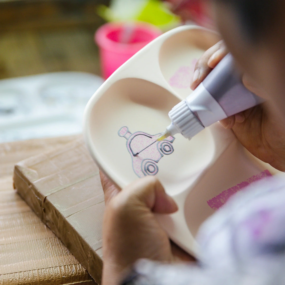 Artisan painting a small car illustration onto a kids section plate with careful hand detailing