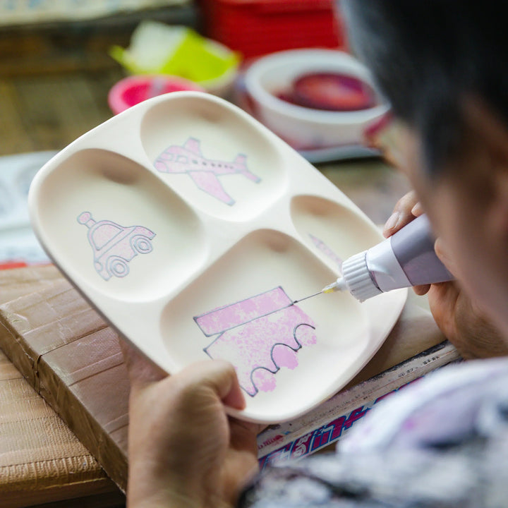 Artisan outlining playful vehicle designs on a kids section plate during the hand painting process